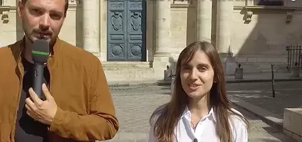 Un homme avec un micro accompagne jeune femme en blanc dans les rues de Paris, au fond une église